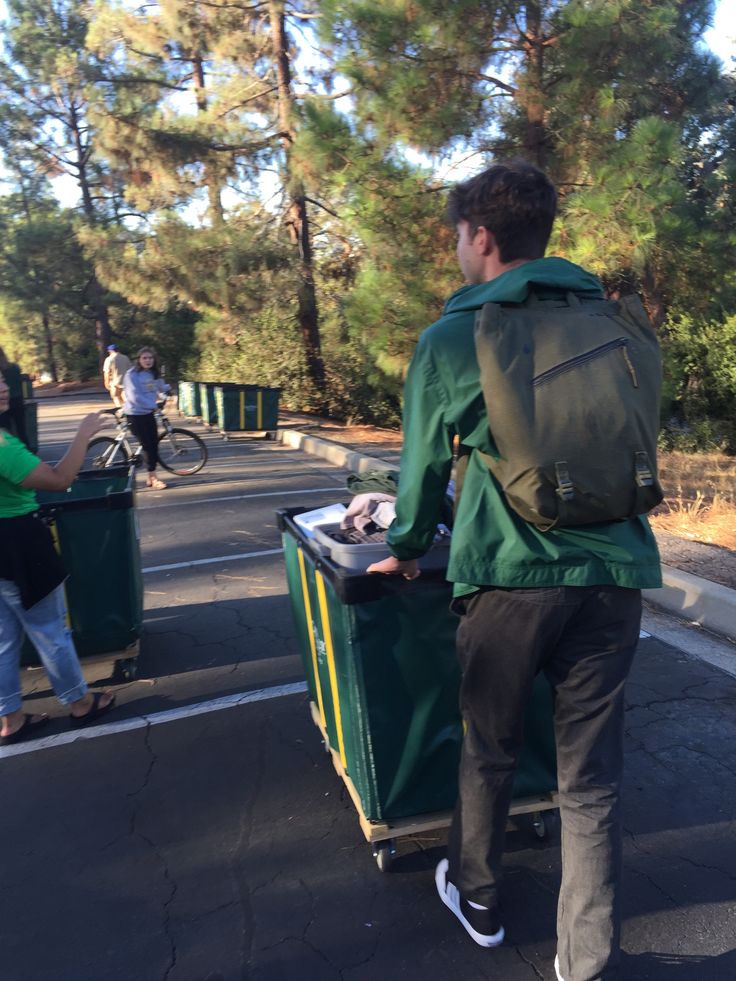 a man with a green backpack is pushing a cart full of garbage down the street