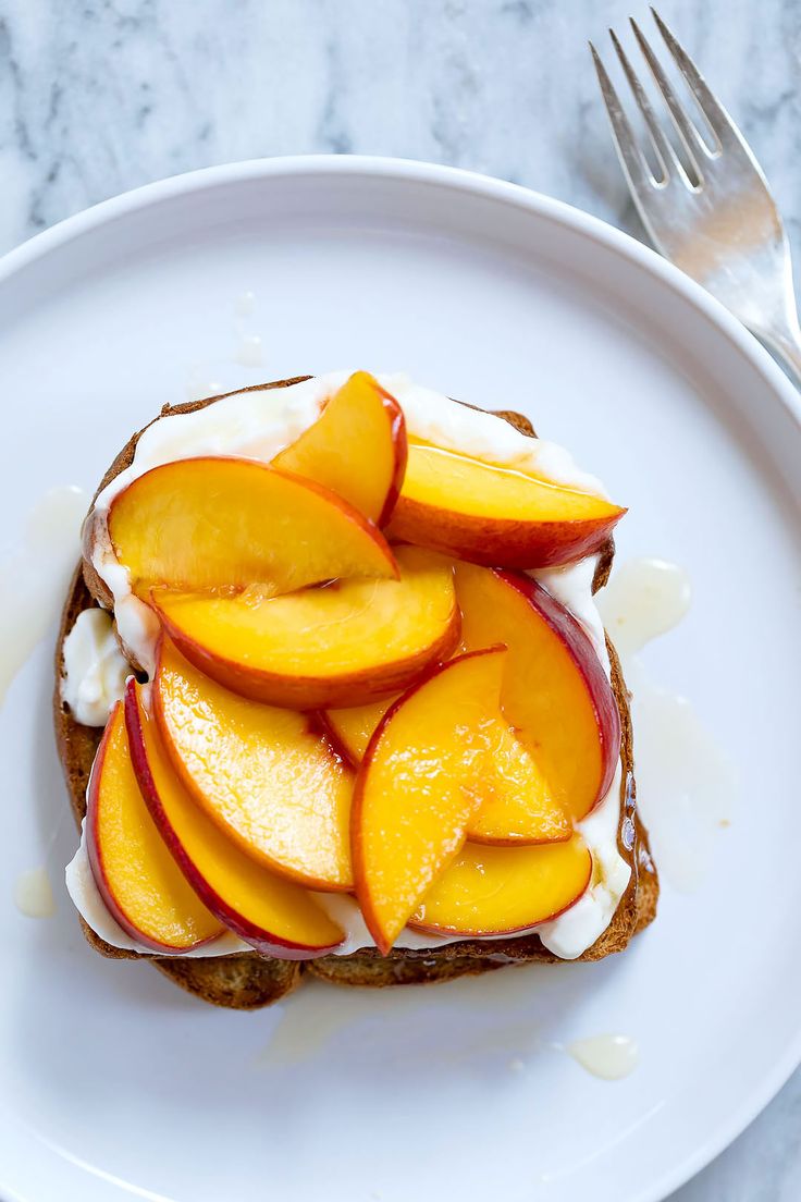 a piece of toast topped with sliced peaches and whipped cream on a white plate