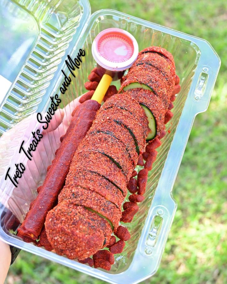 a person holding a plastic container filled with meat and veggie covered hotdogs