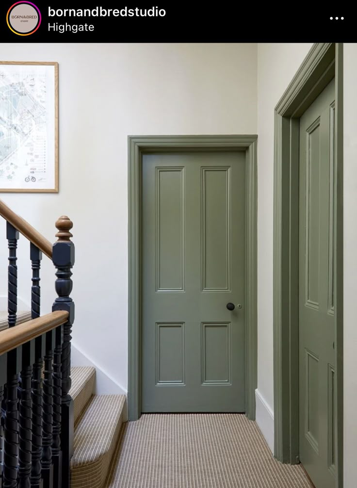 a green door in a white room next to a black banister and stair case