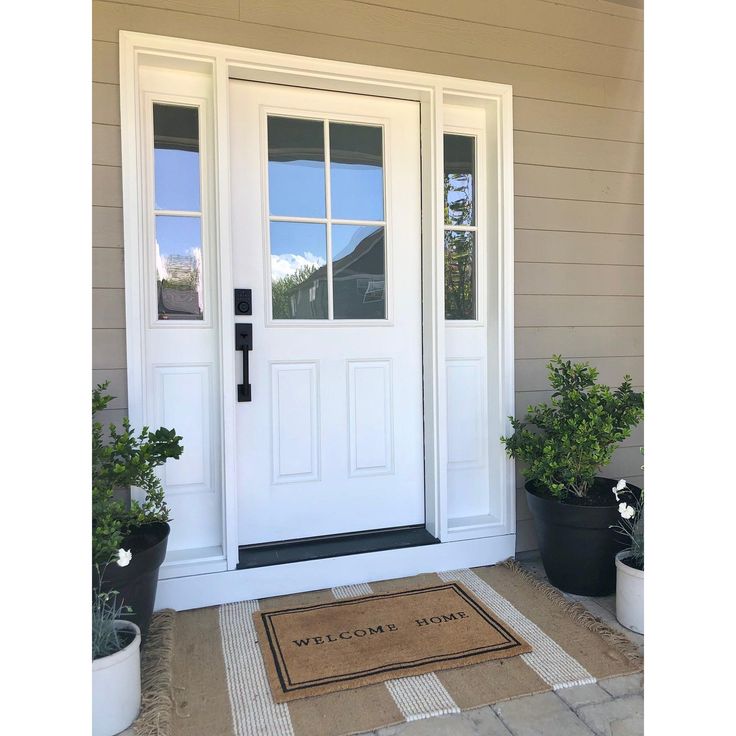 a welcome mat is placed in front of a door with potted plants on the side