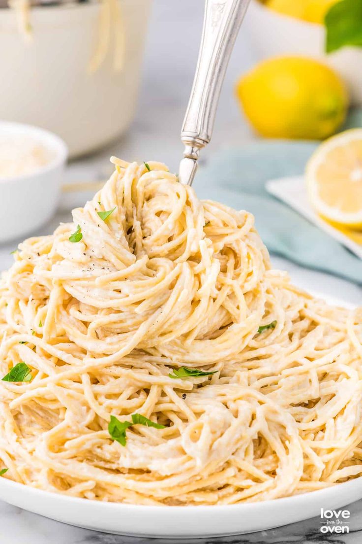 a fork full of spaghetti being lifted from a white bowl with lemons in the background