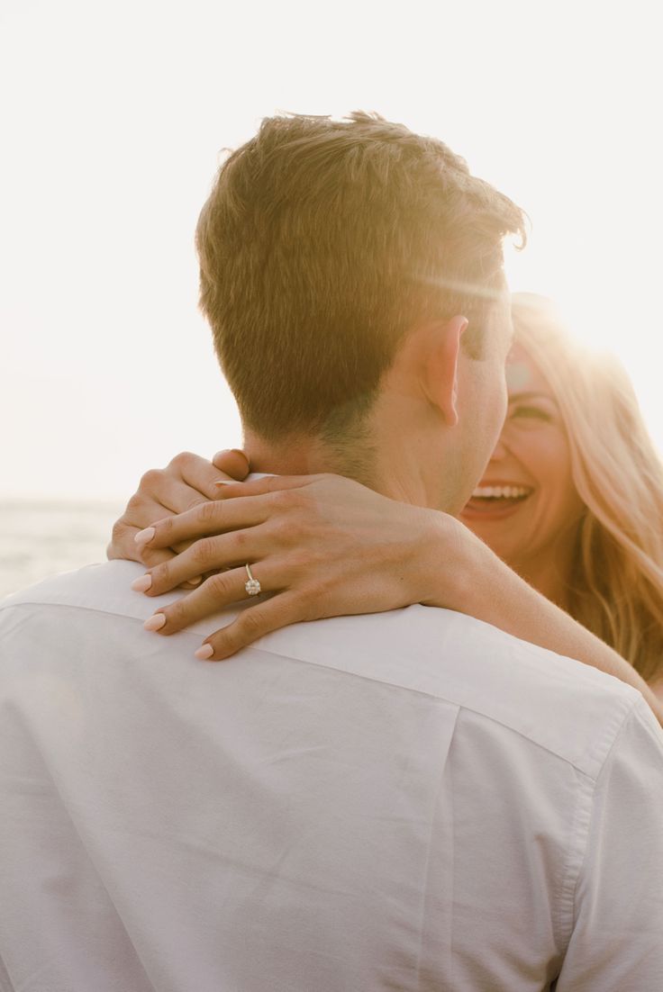 a man and woman embracing each other on the beach with the sun shining behind them