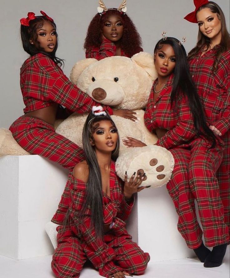 four women in matching red and black pajamas posing with a large teddy bear on their lap