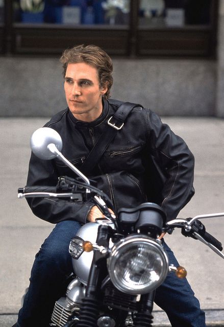 a man riding on the back of a motorcycle down a street next to a building