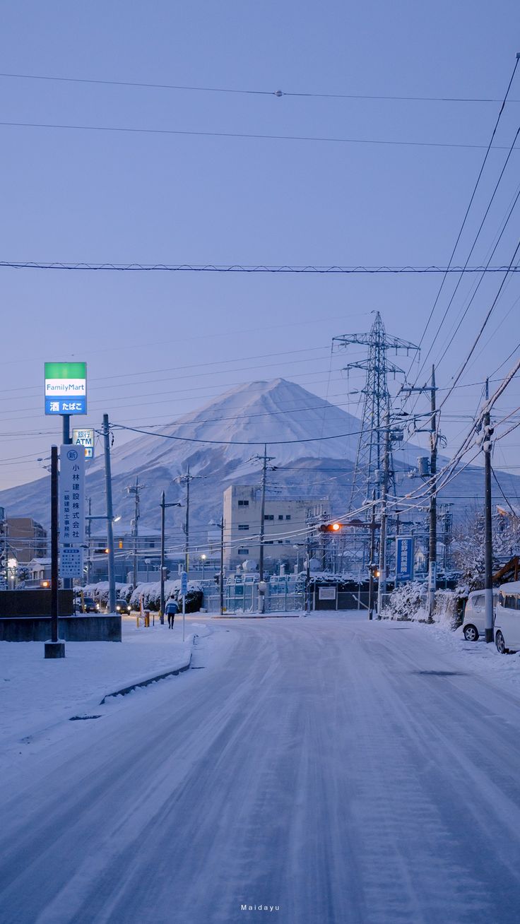 a snowy street with power lines and mountains in the background