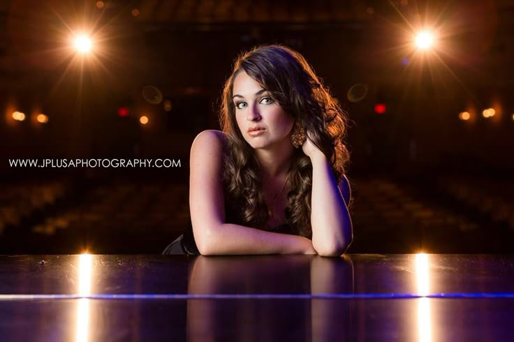 a beautiful young woman sitting on top of a table in front of a stage with bright lights