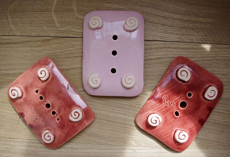 three pink and white ceramic pieces on a wooden floor, one with two holes in the middle