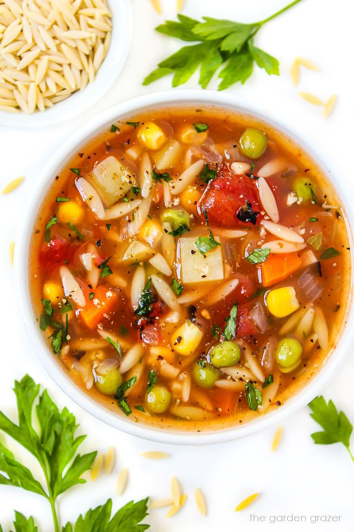 a white bowl filled with vegetable soup next to some parsley