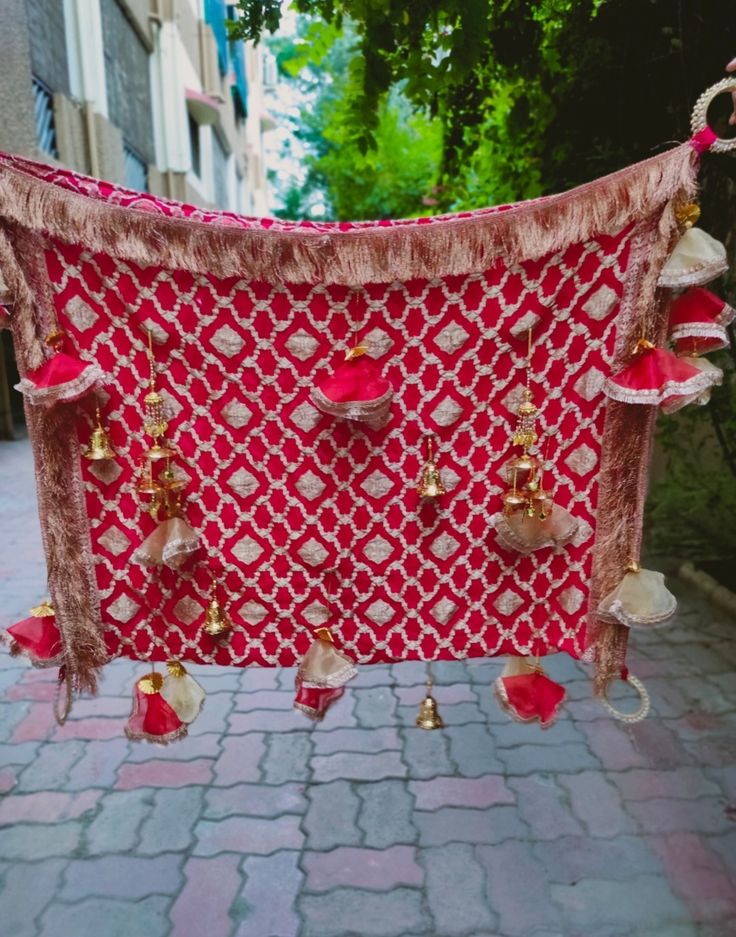 a red and white blanket hanging on a brick sidewalk next to a tree with lots of tassels