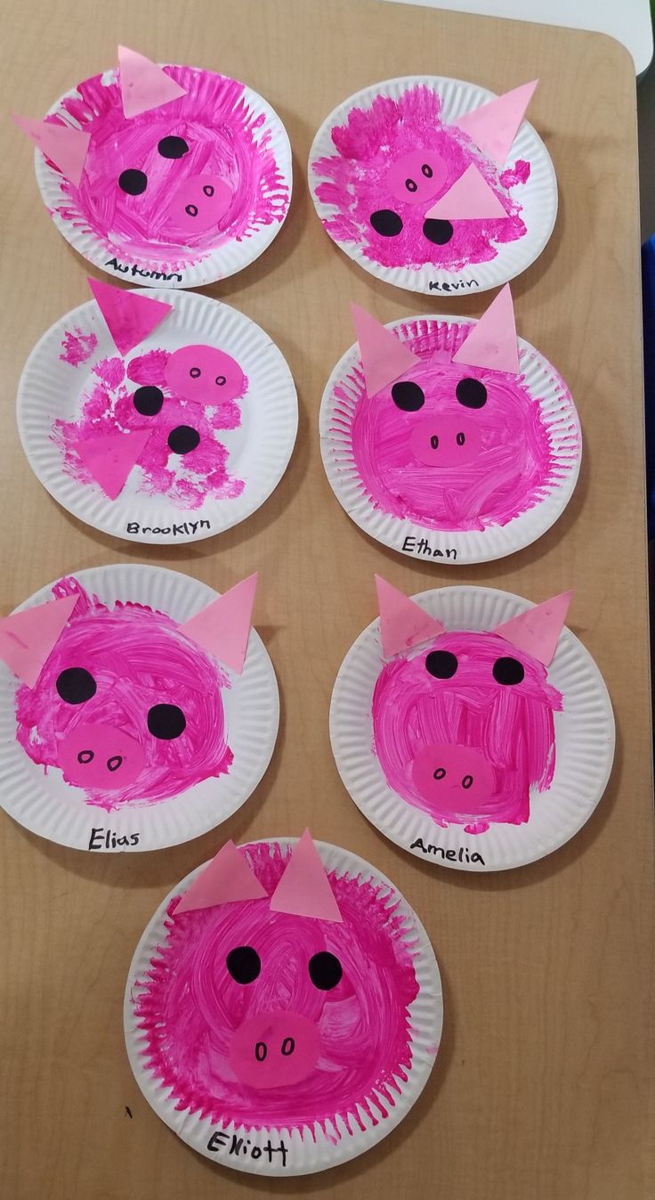 paper plates with pink pigs on them sitting on top of a wooden table next to blue markers