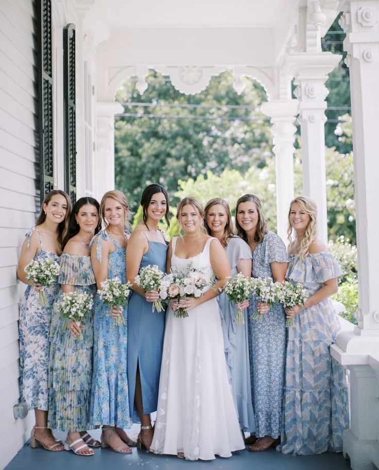 a group of women standing next to each other in front of a white house holding bouquets