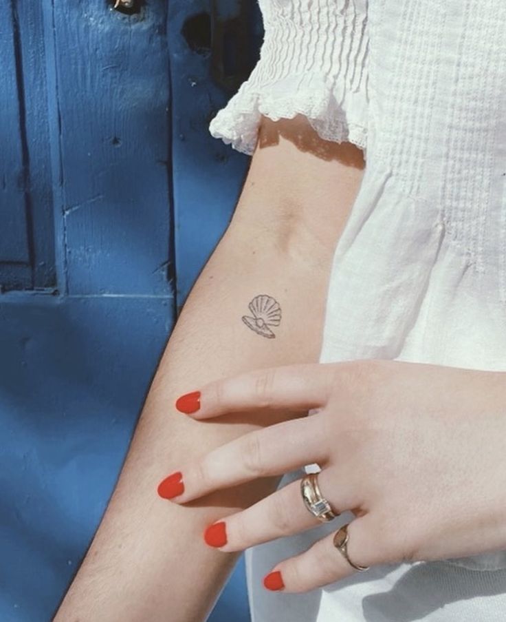 a woman's hand with a small shell tattoo on her left wrist and red nail polish