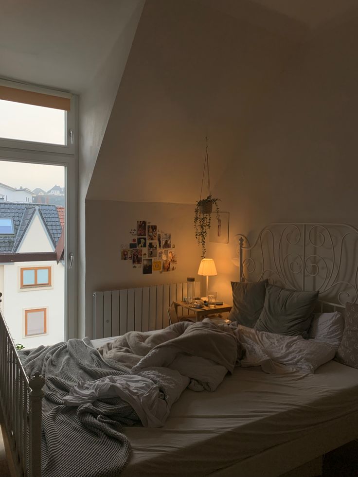 an unmade bed sitting next to a window in a bedroom