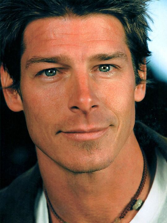 a close up of a person wearing a suit and tie with a necklace on his neck