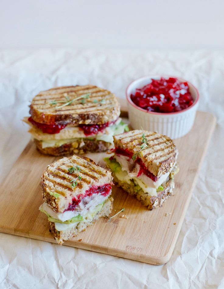 two grilled sandwiches cut in half on a cutting board next to a bowl of cranberry sauce