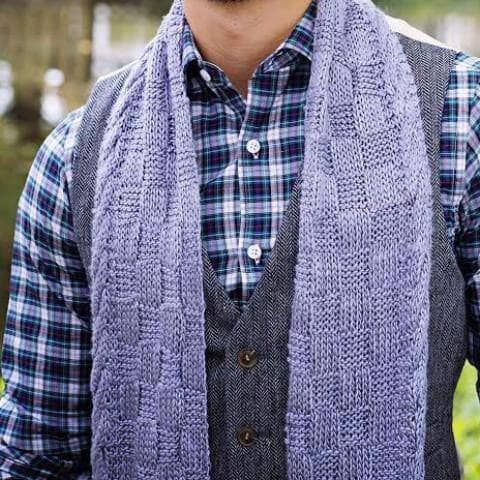 a man wearing a plaid shirt and vest with a knitted scarf around his neck