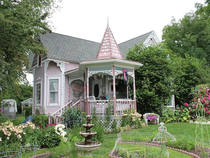 a small pink house with a fountain in the front yard and garden beds around it