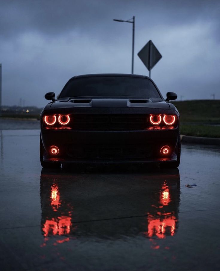 a black car with red lights on it's headlight is parked in the rain