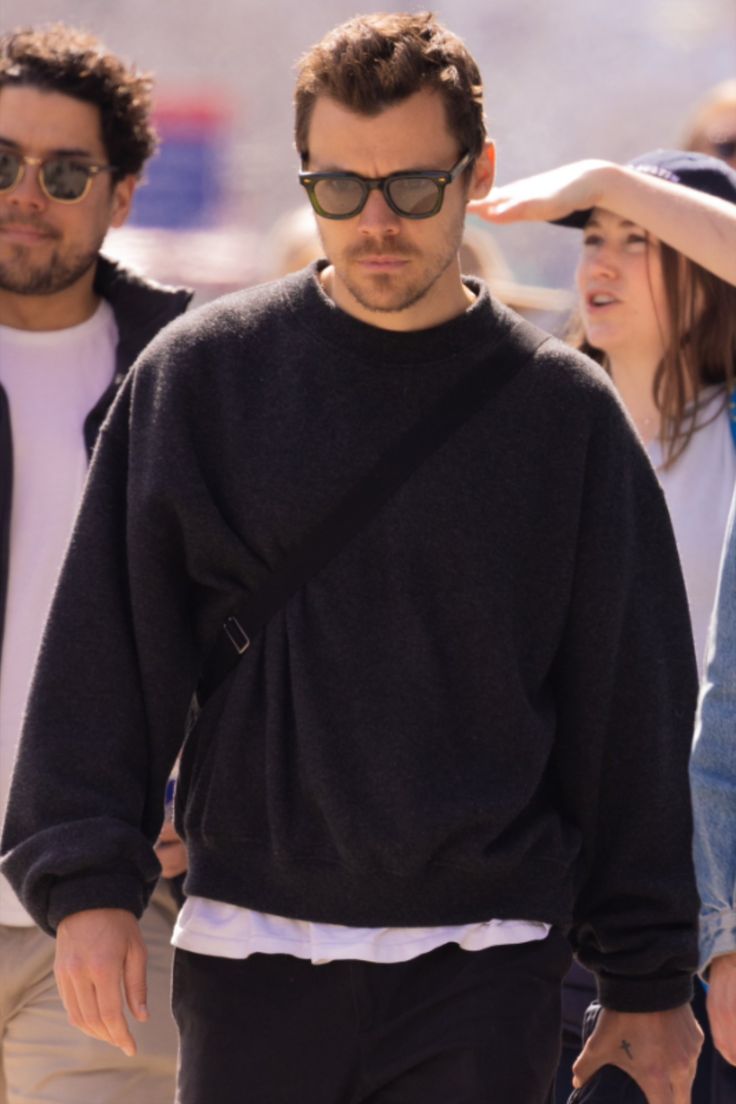 a man in black sweater and sunglasses walking down the street with other people behind him