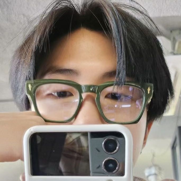 a man with glasses holding up an old camera to take a selfie in front of his face