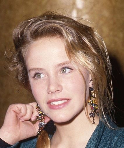 a woman with blonde hair wearing earrings and a blue shirt is posing for the camera