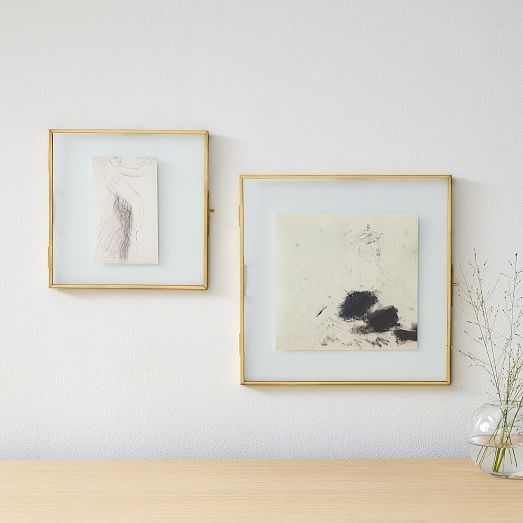 two framed pictures hang on the wall above a wooden table with vases and flowers