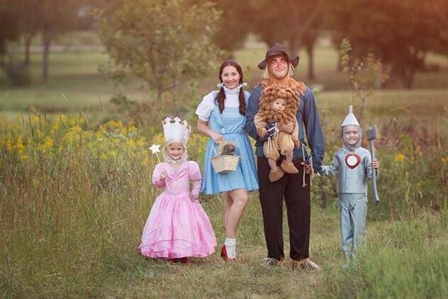 a family dressed up as wizard and princess standing in the grass with two children wearing costumes