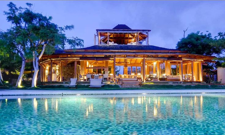 an outdoor pool area next to a house with lights on it and chairs around the pool