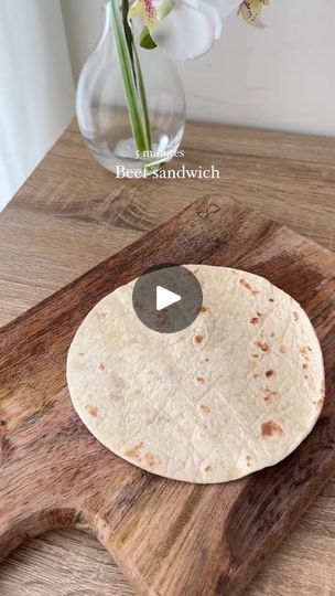 a tortilla sitting on top of a wooden cutting board next to a vase with flowers