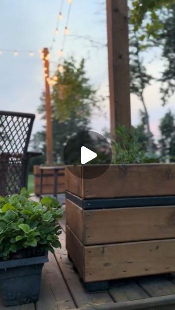 a wooden crate sitting on top of a wooden deck next to two potted plants