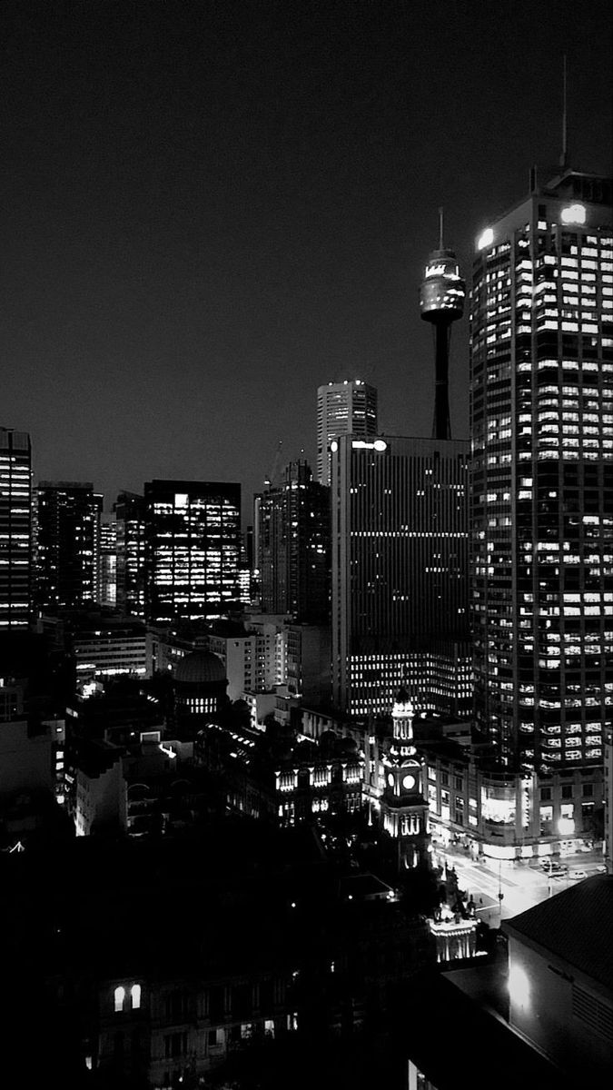 black and white photograph of city skyline at night with lights on the buildings in the foreground