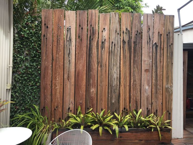 a wooden fence is next to some plants and a table with a chair on it