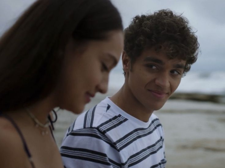 two people standing next to each other near the ocean