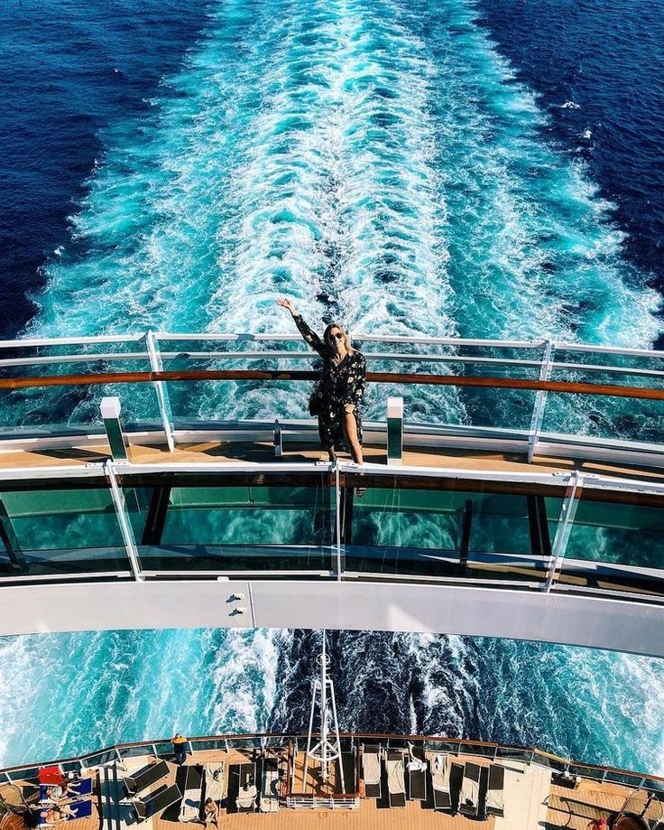 a person standing on the back of a boat in the ocean with their arms up