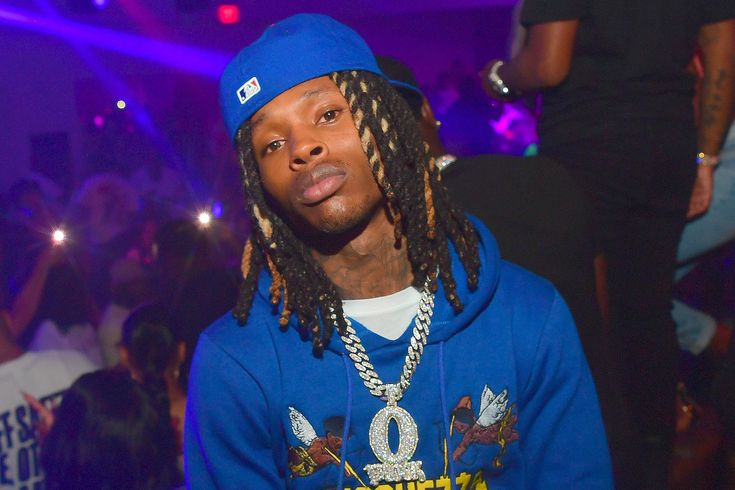 a young man with dreadlocks and a blue hoodie standing in front of a crowd