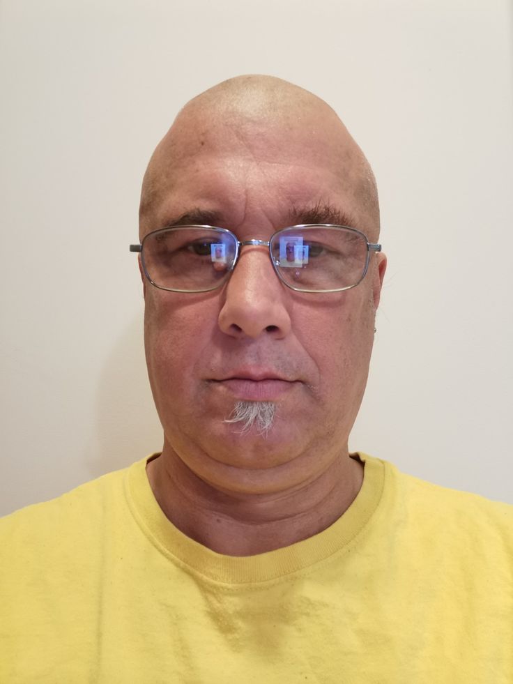 a bald man with glasses and a moustache on his face looking at the camera