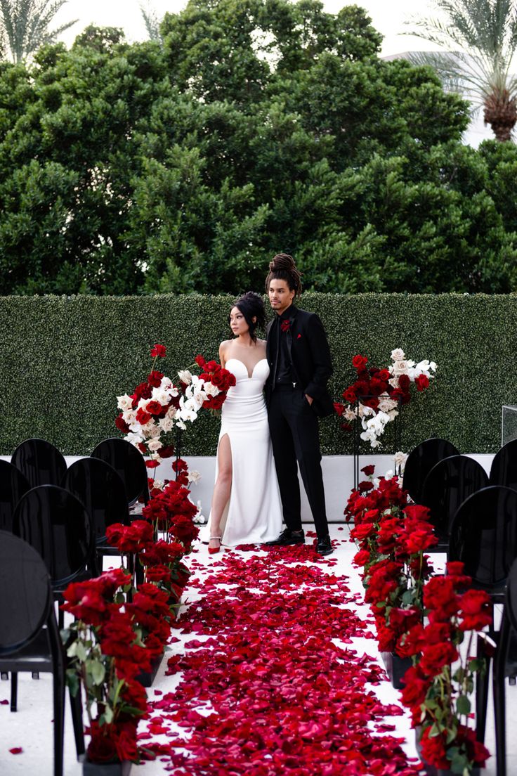 a man and woman standing in front of an aisle with flowers on the ground next to them