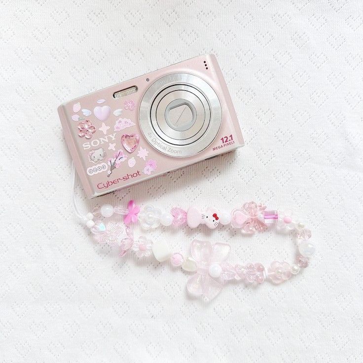 a pink camera sitting on top of a white table next to a bracelet and necklace