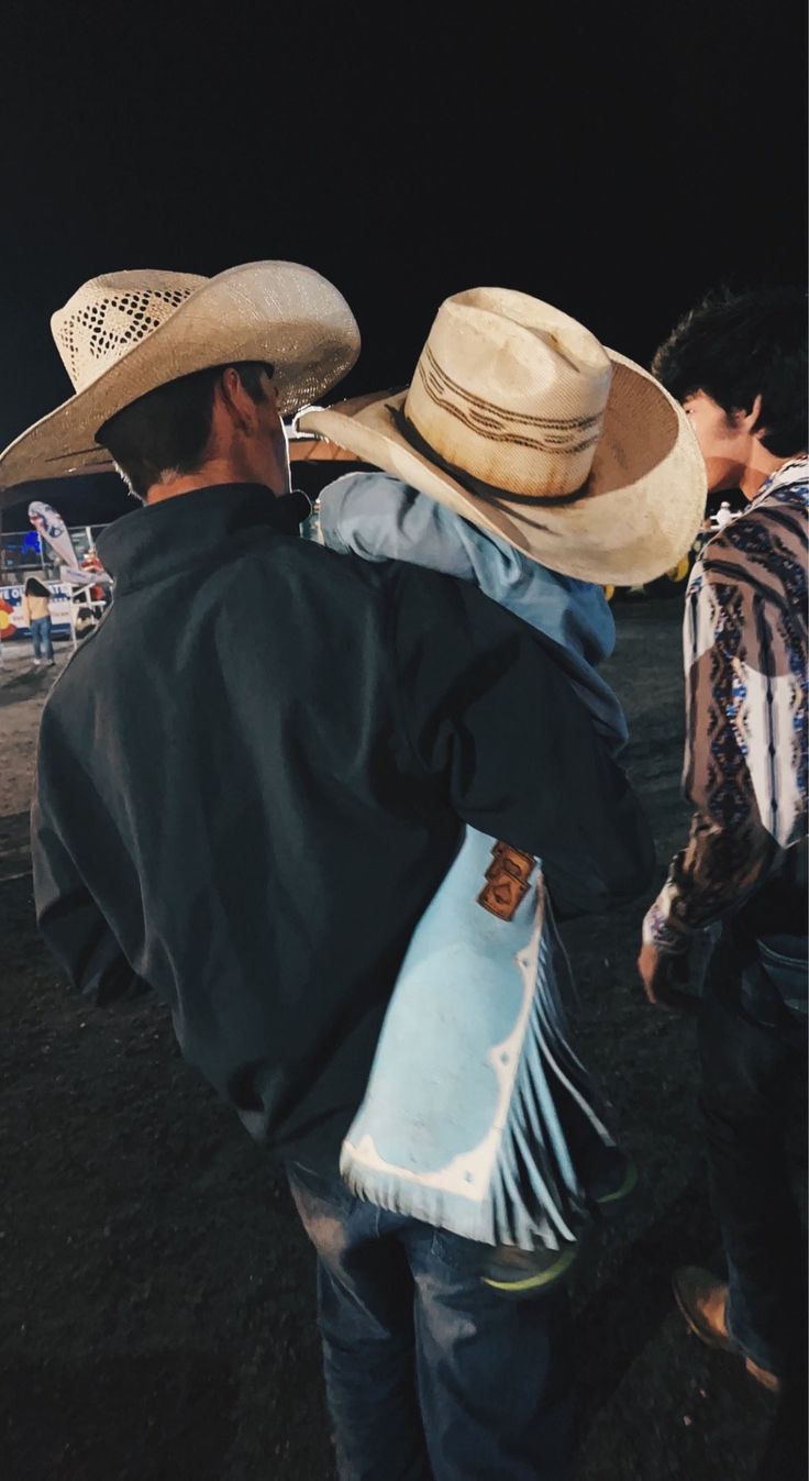 two men in cowboy hats walking on the beach at night with their backs to each other