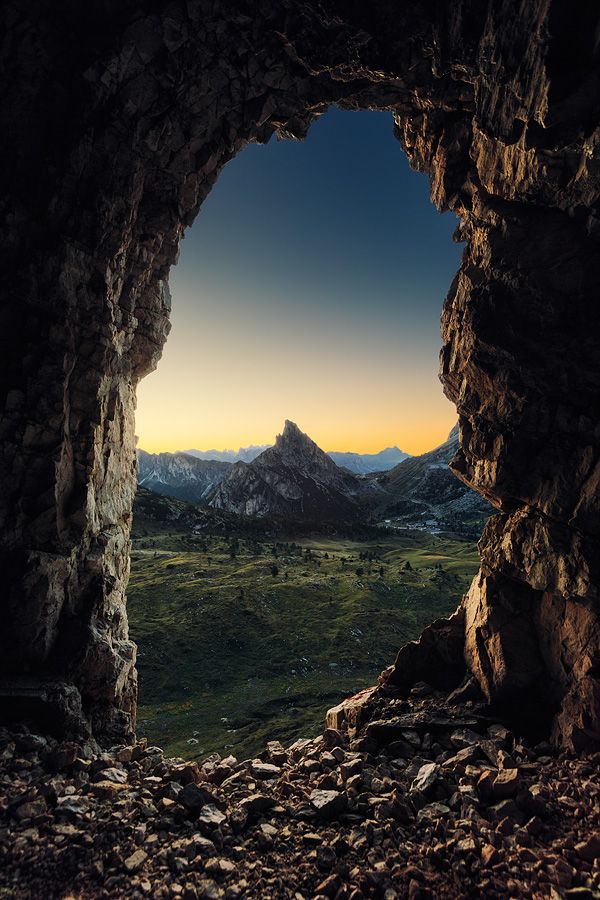 an open cave with the sun setting in the distance, and mountains in the background