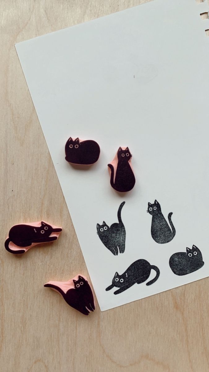 three black cats and one pink cat on a white sheet of paper next to some metal magnets