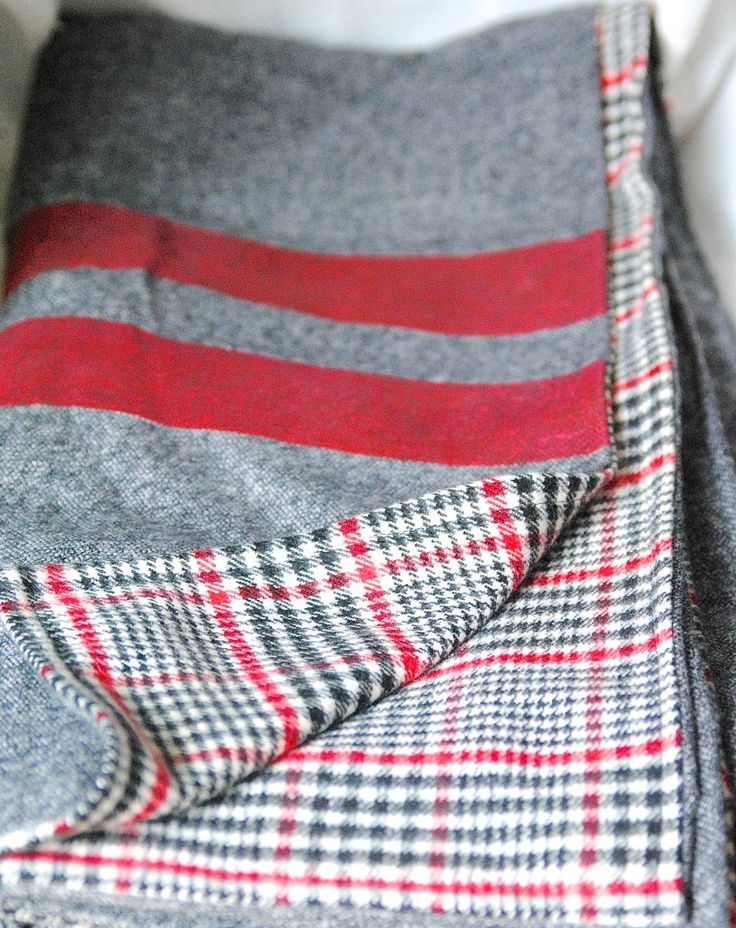 a red and grey blanket laying on top of a bed next to a white pillow