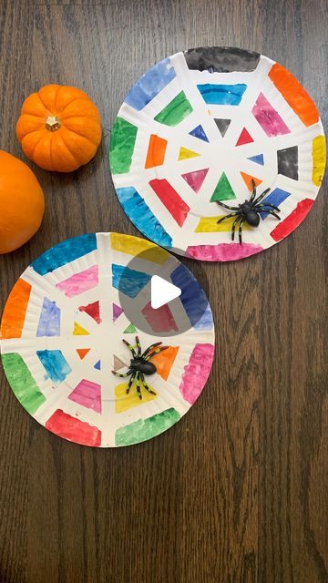 two paper plates with spider designs on them next to an orange and some pumpkins