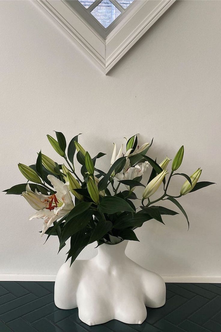 a vase with flowers in it sitting on a table next to a wall and window