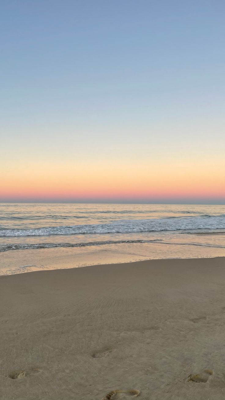 footprints in the sand on a beach at sunset with waves coming in from the ocean