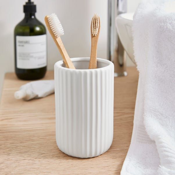 two toothbrushes in a white cup on a wooden table next to a bottle