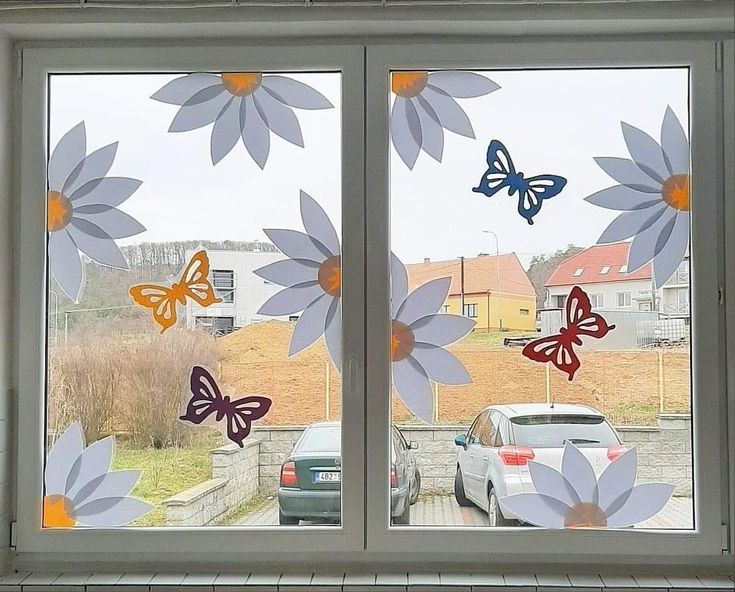 a window with butterflies on it and cars parked in the street behind them, as seen from outside