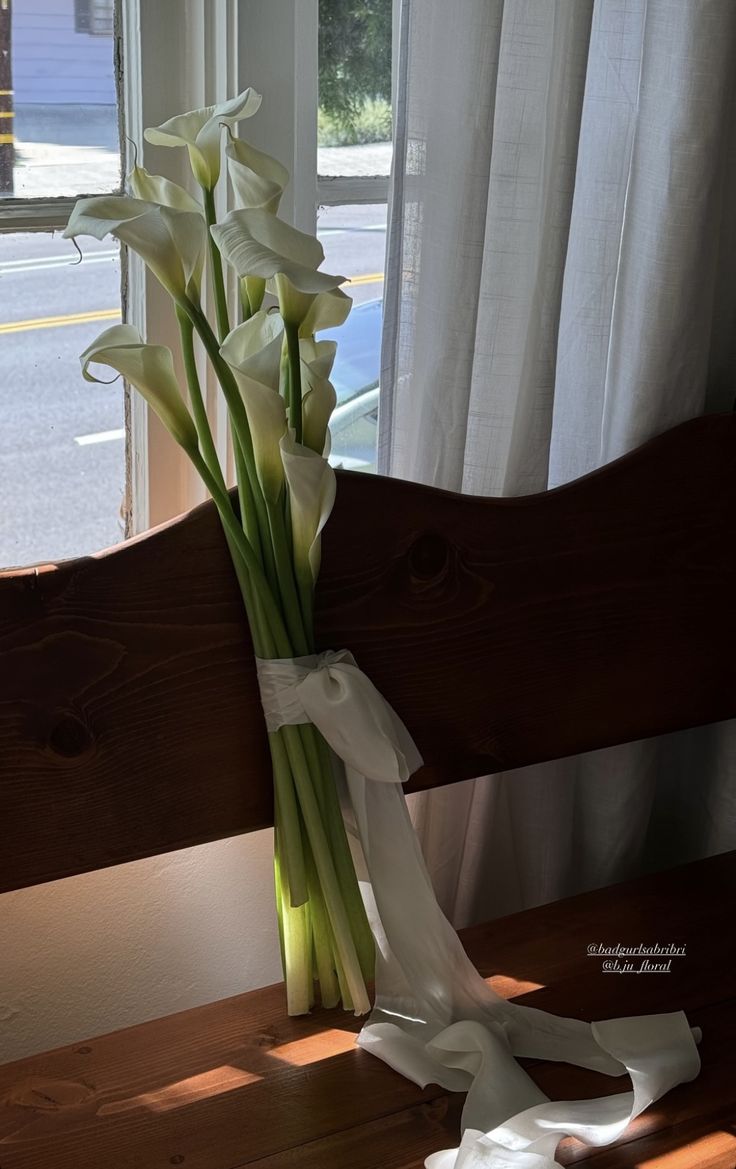 a bouquet of white flowers sitting on top of a wooden bench next to a window