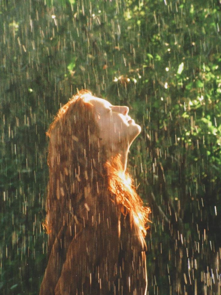 a woman is standing in the rain with her head turned to look up at something